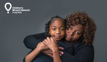 Mother-daughter portrait on grey backdrop with white Children's Miracle Network logo in the left corner