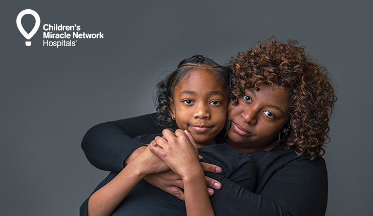 Mother-daughter portrait on grey backdrop with white Children's Miracle Network logo in the left corner