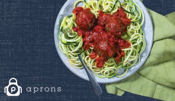 Plate of pasta and meatballs on blue denim background with the white Publix Aprons logo