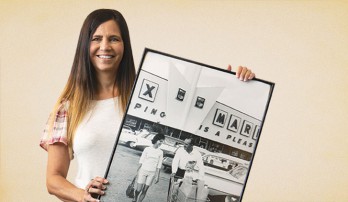 Publix associate holds a black and white image of Mr. George and a lady with a baby in a shopping cart above groceries.