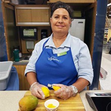 Publix Associate Colleen Whitlow stands at a food prep station holding a lemon and lemon peeler.