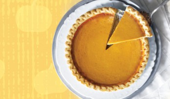 Overview shot of a pumpkin pie on a white plate, with a slice being taken out.